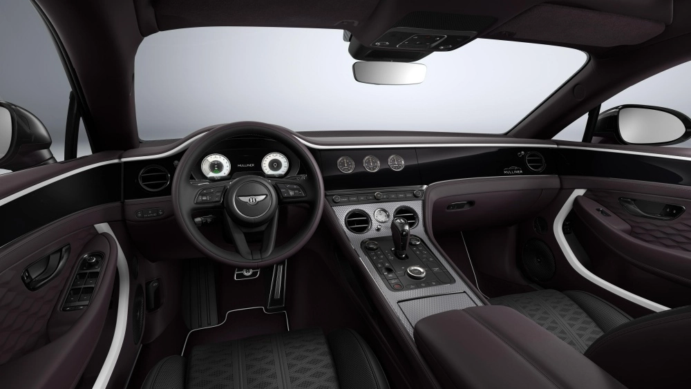 Bentley Continental GT'nin sürücü koltuğundan görünen bu geniş açılı çekimde, mor deri döşemelerle süslenmiş lüks iç mekan tasarımı dikkat çekiyor; direksiyon, dijital göstergeler, ortadaki şık kontrol paneli ve kapı içi detaylar, aracın modern ve sofistike atmosferini gözler önüne seriyor.