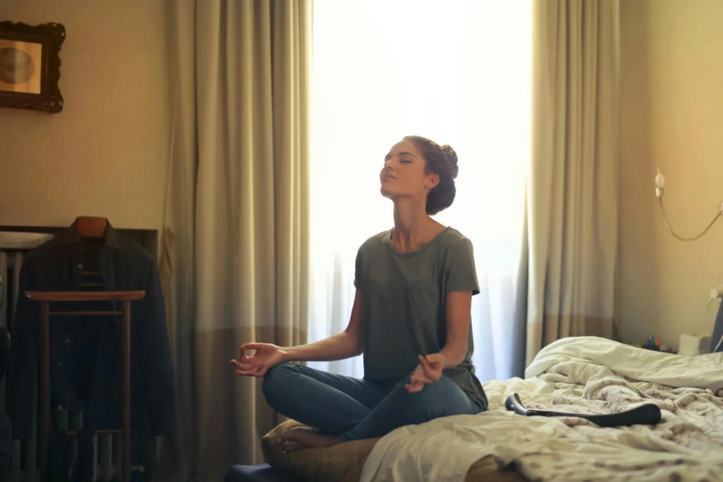 Yatak odasında sabah meditasyonu yapan kadın, dinginlik ve iç huzur arayışında.