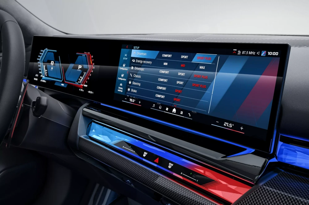 BMW M5 Sedan'ın iç mekanındaki geniş infotainment ekranında, SPORT PLUS modu seçili sürüş ve enerji geri kazanım ayarları gösterilirken, ekranın altındaki mavi-kırmızı aydınlatmalı ve karbon fiber detaylı kontrol paneli bu plug-in hibrit otomobilin gelişmiş iç mekan tasarımını gözler önüne seriyor.