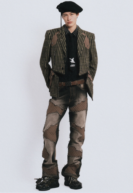 Genç bir erkek model, Off-White'ın cesur estetiğini yansıtan, dik omuzlu ekose kısa bir ceket, saplamalı yakası olan siyah bir gömlek, kravat, kahverengi bir kemer ve kapitone yamalı koyu renk pantolon ile siyah bir bere ve detaylı ayakkabılar giyerek modern erkek giyim dünyasının yenilikçi trendlerini sergiliyor.