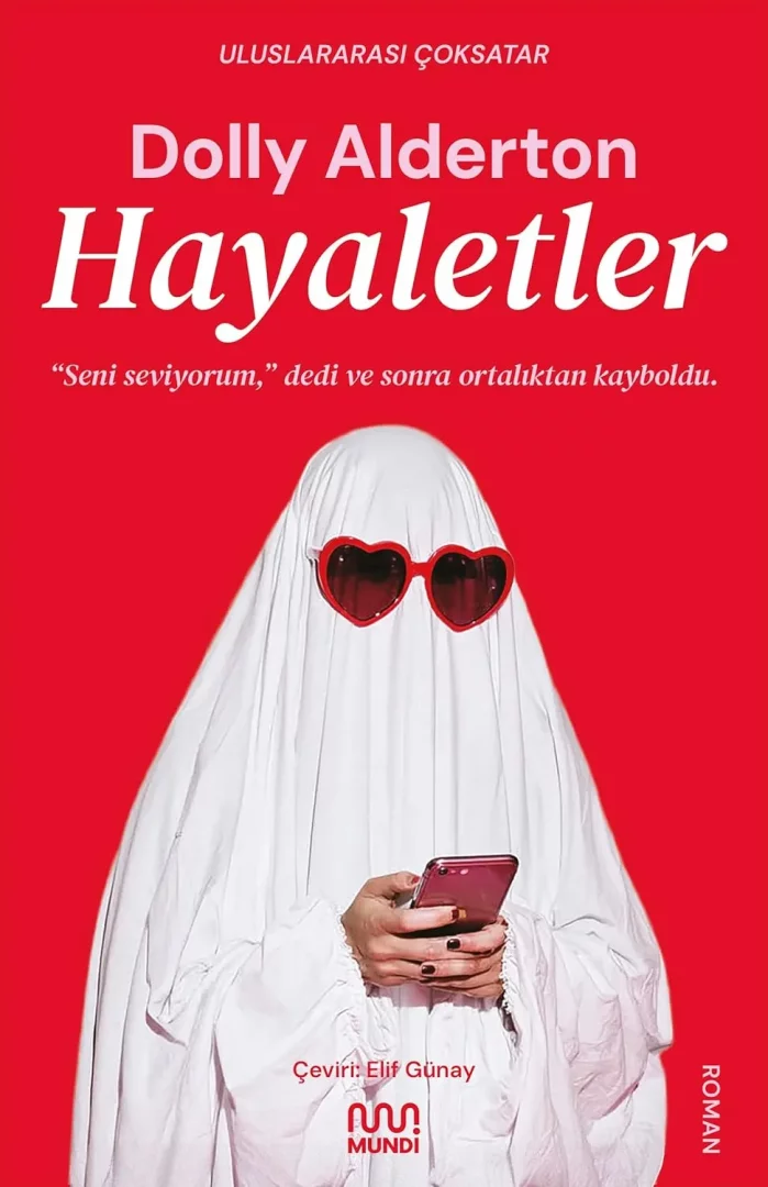 Kırmızı bir arka plan üzerinde, beyaz çarşafla hayalet kostümü giymiş, kalp şekilli kırmızı gözlük takan ve akıllı telefonuna bakan bir figür, Dolly Alderton'ın sürükleyici Hayaletler romanının dikkat çekici kapağını oluşturuyor, okuyuculara deniz kenarı için ilginç bir kitap önerisi sunuyor.