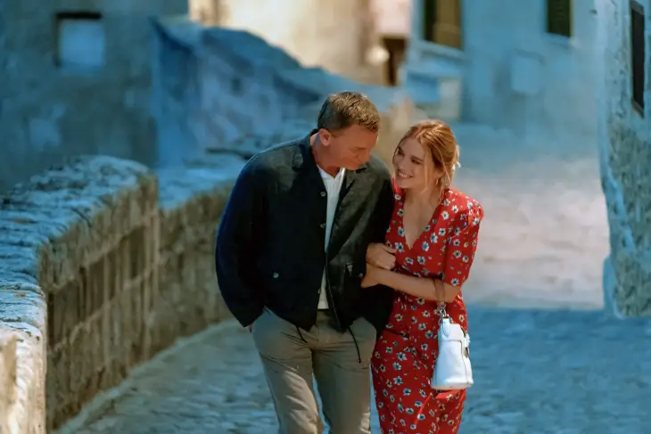 Daniel Craig'in hayat verdiği James Bond, tarihi bir kasabanın dar sokaklarında partneriyle kol kola neşeyle yürürken, lacivert blazer ceketi, beyaz tişörtü ve açık renk pantolonuyla James Bond stilinin günlük ama karizmatik şıklığını gözler önüne seriyor.