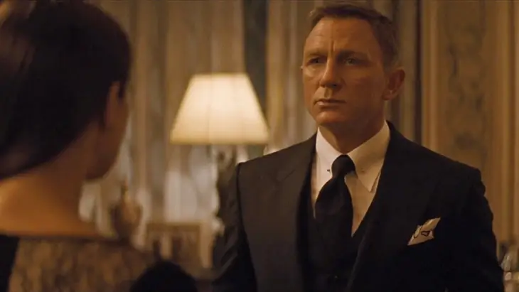 Daniel Craig'in canlandırdığı James Bond, beyaz gömleği, koyu renk kravatı ve cep mendiliyle tamamladığı kusursuz kesimli koyu renk takım elbisesiyle, postun vurguladığı zamansız James Bond stilinin sofistike ve karizmatik duruşunu başarıyla sergiliyor.