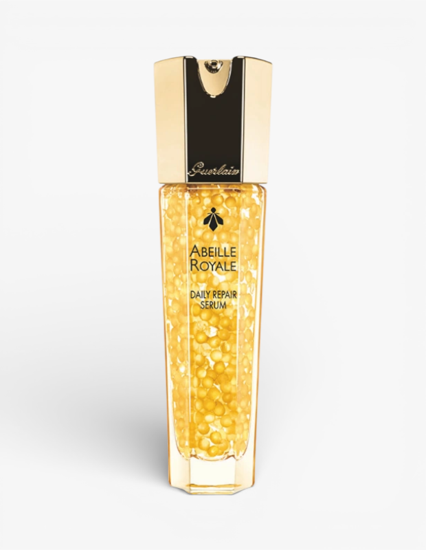 Kadınlar için lüks bir Sevgililer Günü hediyesi olan Guerlain Abeille Royale Daily Repair Serum, bal rengi mikro boncuklarla dolu cam şişesi ve altın rengi şık kapağıyla beyaz fonda duruyor.