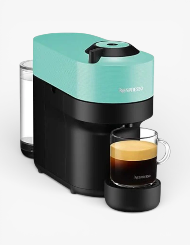 Kadınlar için Sevgililer Günü hediye fikri olan turkuaz kapaklı, siyah gövdeli modern Nespresso kahve makinesi, cam fincandaki taze ve köpüklü espresso ile sergileniyor.