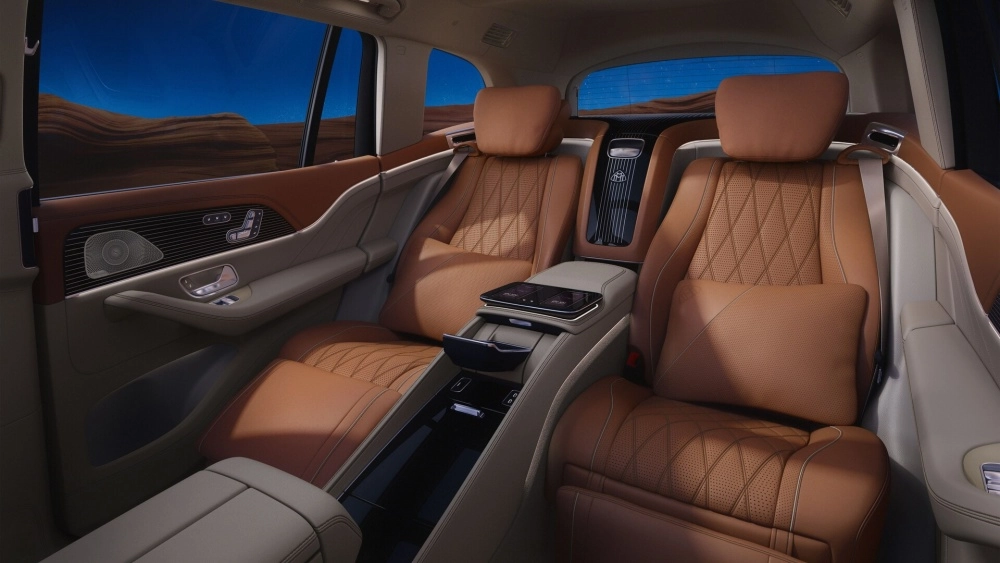 Mercedes-Maybach GLS'in arka koltuk makam bölümünün lüks iç mekan tasarımı, baklava desenli ve delikli açık kahverengi deri döşemeler, iki koltuk arasındaki geniş merkezi konsolunda yer alan ekranlar ve pencereden görünen dağlık çöl manzarasıyla konfor ve şıklığı birleştiriyor.