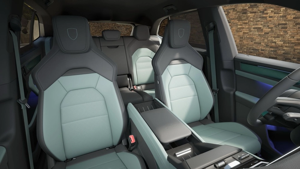 Porsche Cayenne Turbo Electric elektrikli SUV modelinin ferah iç mekanında, mint yeşili ve koyu gri renkteki delikli deri koltuklar, markanın logosu işlenmiş başlıklar ve mavi ambiyans aydınlatması modern tasarımını vurguluyor.