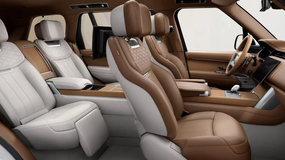 Range Rover SV'nin açık kahve ve krem renkli delikli deri döşemelere, zarif ahşap kaplamalara ve arka yolcular için entegre ekranlara sahip lüks iç mekan tasarımı, modern SUV konforunu ve premium detay işçiliğini gözler önüne seriyor.