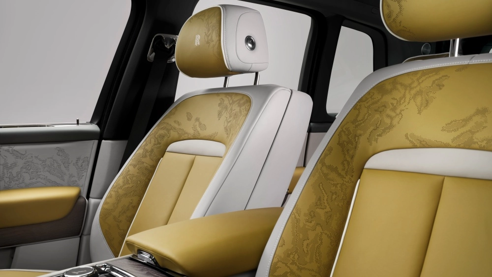 Rolls-Royce Cullinan Series 2 lüks SUV'un zarif iç mekan tasarımında, altın sarısı ve krem beyazı deri koltuklar, detaylı ve karmaşık desenleriyle dikkat çekerek yolcu bölmesine sofistike bir hava katıyor.