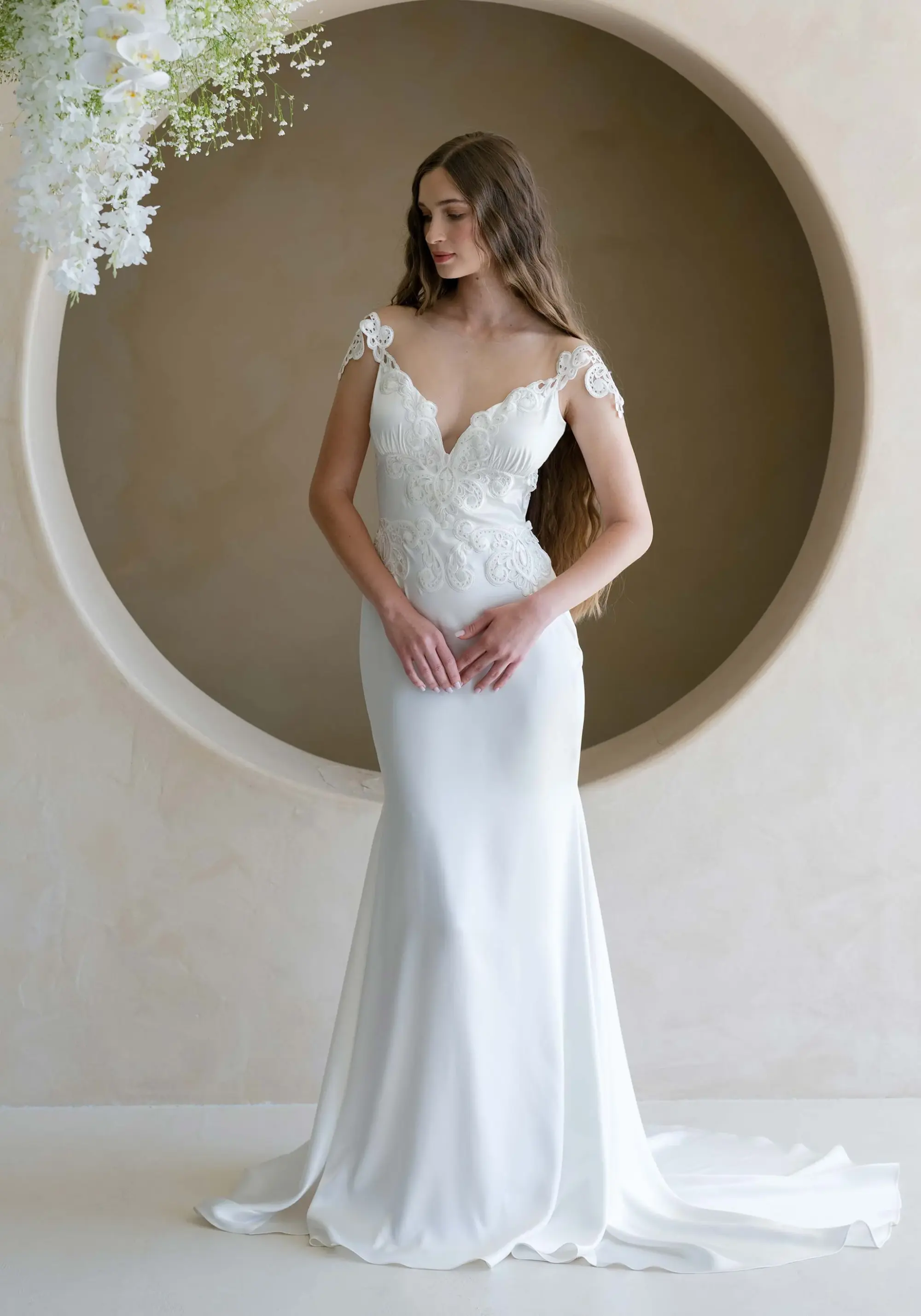 V yaka, ince askılı Claire Pettibone gelinlik; üst bedende zarif dantel aplikeler ve düz, akıcı etekle minimal ve modern bir görünüm.