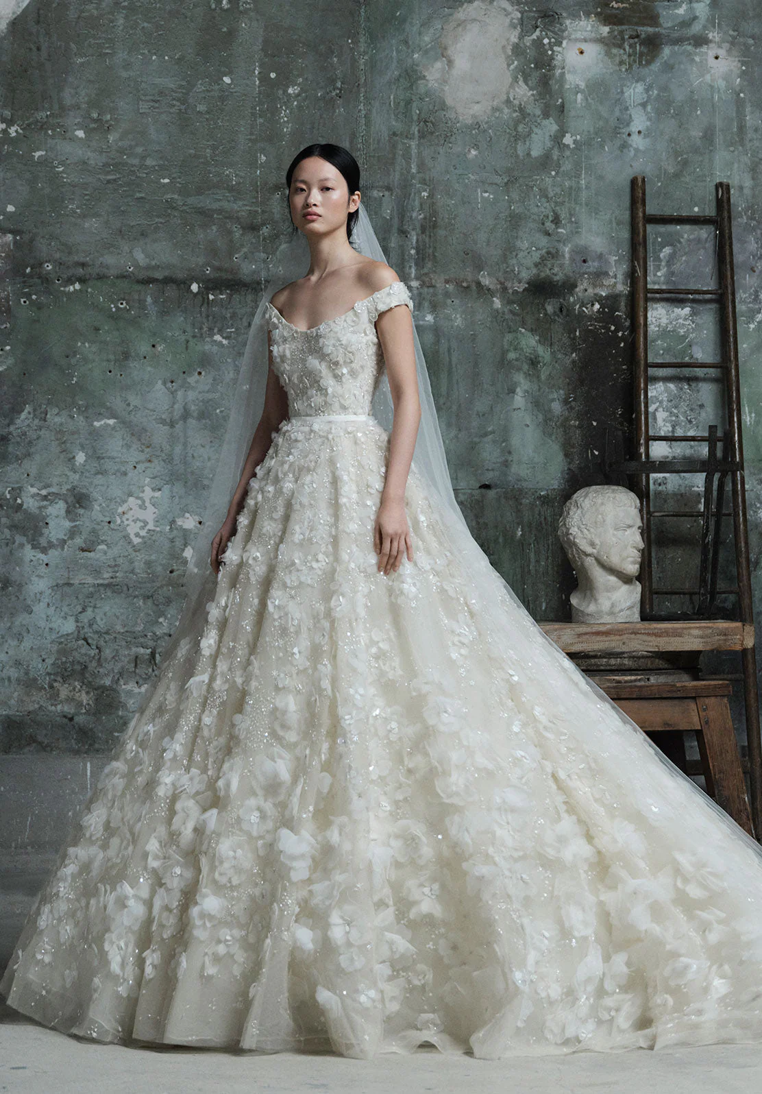 Elie Saab 2026 ilkbahar koleksiyonundan üç boyutlu çiçek işlemeli, düşük omuzlu romantik balo tipi gelinlik.