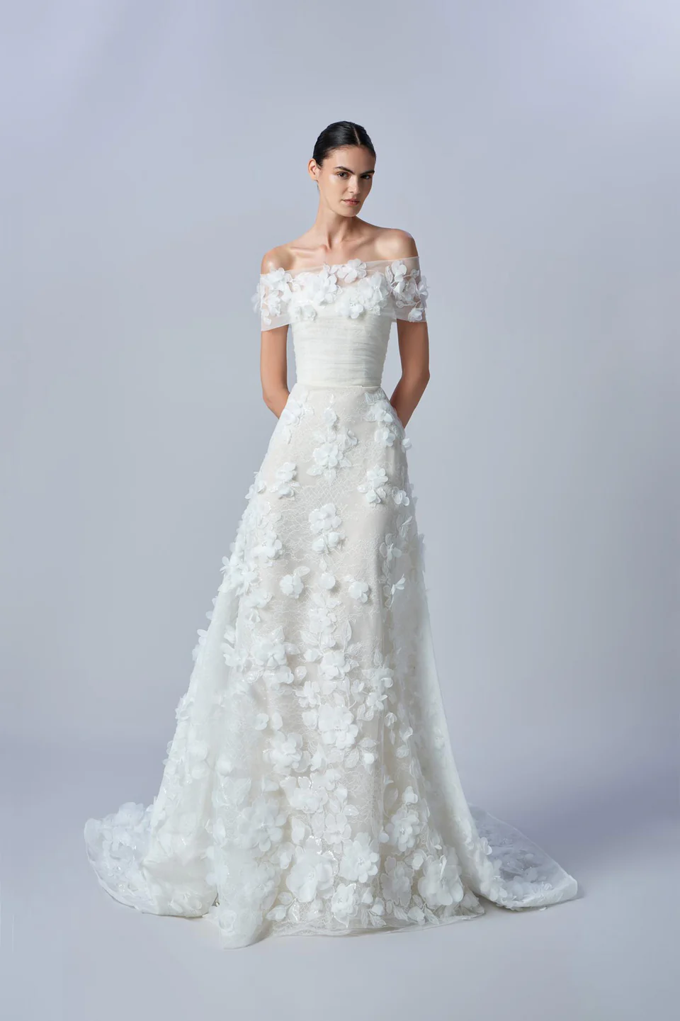 Elie Saab 2026 sonbahar koleksiyonundan düşük omuzlu, üç boyutlu çiçek aplikeli, zarif ve modern romantik gelinlik.