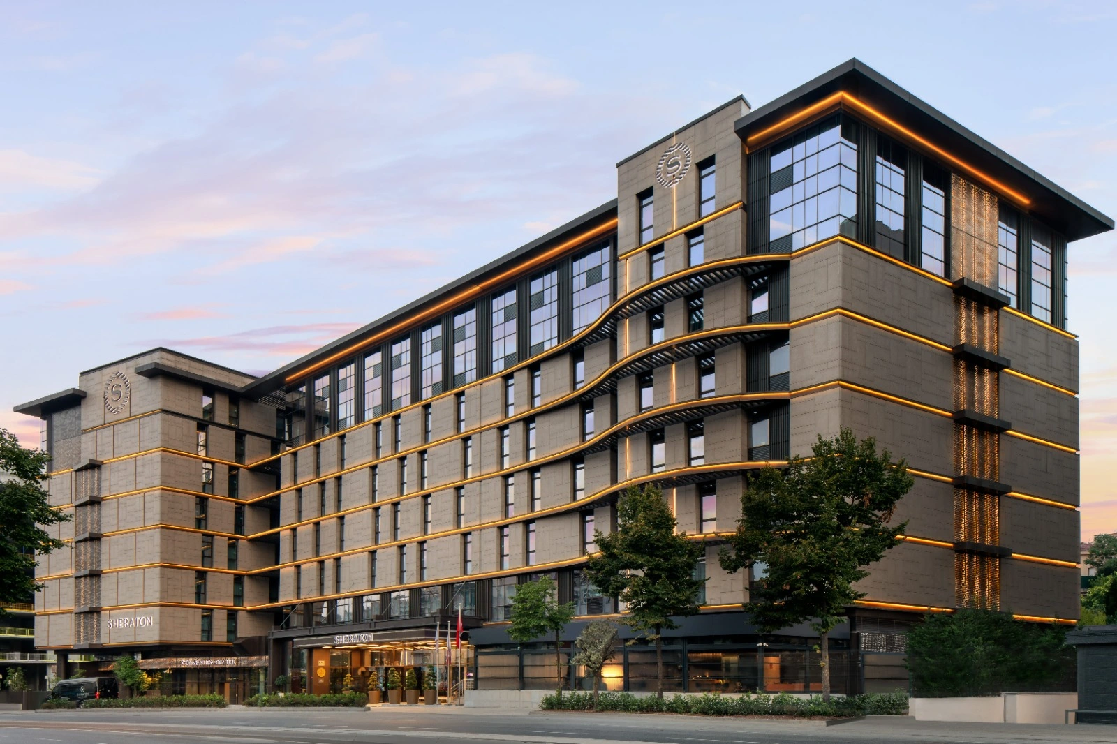 Sheraton İstanbul City Center'ın modern mimarisi, şık taş cephesi ve cephesini çevreleyen altın renkli ışık şeritleriyle akşamüstü gökyüzü altında gösterişli bir duruş sergilerken, bu merkezi otel çiftlere hayallerindeki kişiselleştirilmiş düğün deneyimini sunuyor.