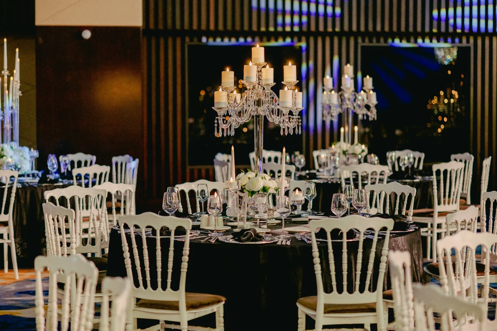 Sheraton Istanbul City Center'ın geniş balo salonunda, siyah masa örtüleri, beyaz Tiffany sandalyeler, masaların ortasında yanan mumlarla süslü gösterişli kristal şamdanlar ve beyaz çiçek aranjmanlarıyla, çiftlerin hayalindeki kişiselleştirilmiş düğün için şık ve zarif bir kutlama ortamı hazırlanmış.