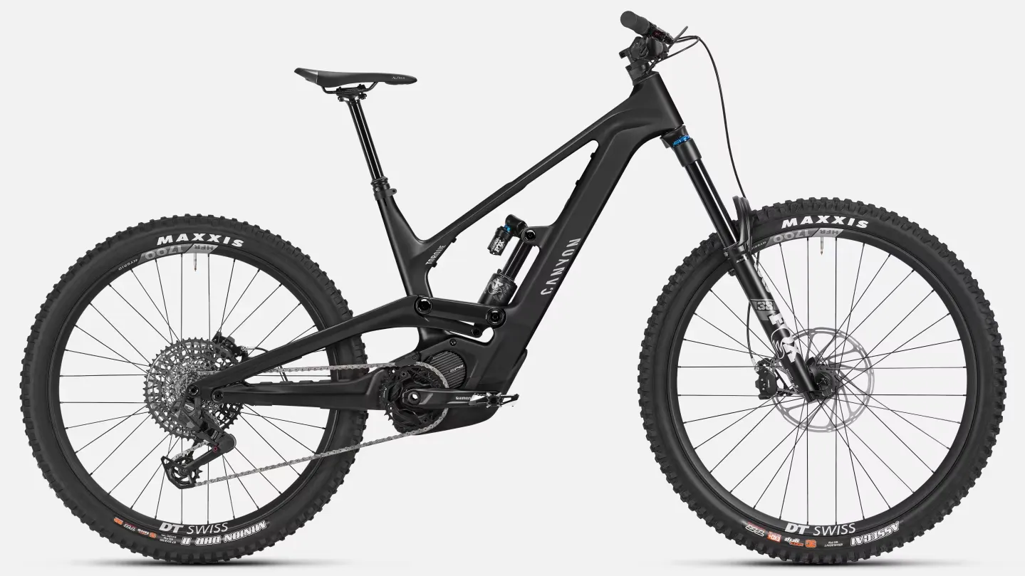 Mat siyah renkte, karbon fiber kadroya sahip, Canyon markasının Torque:ON CF 9 elektrikli dağ bisikleti, entegre motoru, geniş dişli lastikleri, Fox süspansiyonu ve DT Swiss jantlarıyla zorlu arazi koşullarına hazır, dinamik bir görünüm sergiliyor.