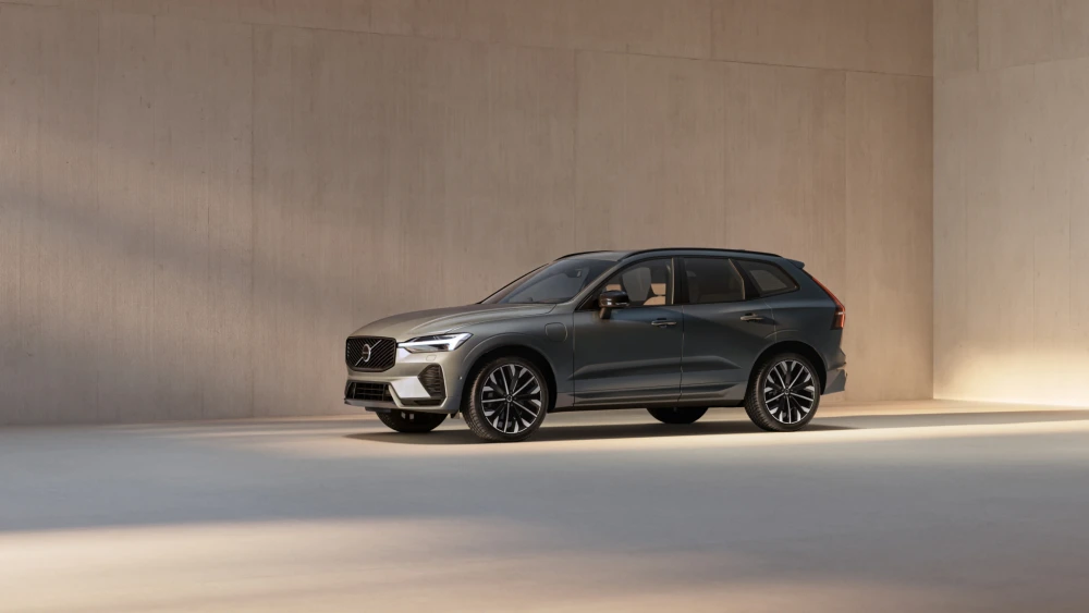 Gri renkli, modern ve zarif dış tasarıma sahip Volvo XC60 T8 AWD şarj edilebilir hibrit otomobil, sade bir iç mekanda yan açıyla park edilmiş olarak görülüyor, ön çamurluktaki şarj portu kolayca fark ediliyor.
