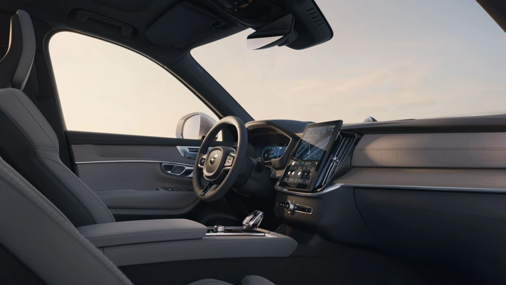Volvo XC90 T8 AWD Plug-in Hybrid şarj edilebilir hibrit otomobilin iç mekan tasarımı, sürücü koltuğundan görünen, açık renk deri döşemeli modern kabini, minimalist tasarımlı direksiyonu ve büyük dikey dokunmatik multimedya ekranıyla konforlu ve teknolojik bir deneyim sunuyor.