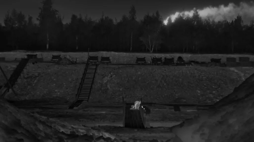 The Zone of Interest (İlgi Alanı) filminden siyah-beyaz sahne: Karanlık bir ormanın önünde, derin bir çukur ve çevresinde ahşap merdivenler ile çeşitli kamp yapıları yer almakta. Çukurun dibinde, evin küçük kızı toplama kampına şeker dağıtıyor. Sahne soğuk, sessiz ve rahatsız edici bir atmosfer taşıyor; savaş suçlarının işlendiği bir toplama kampını simgeliyor.