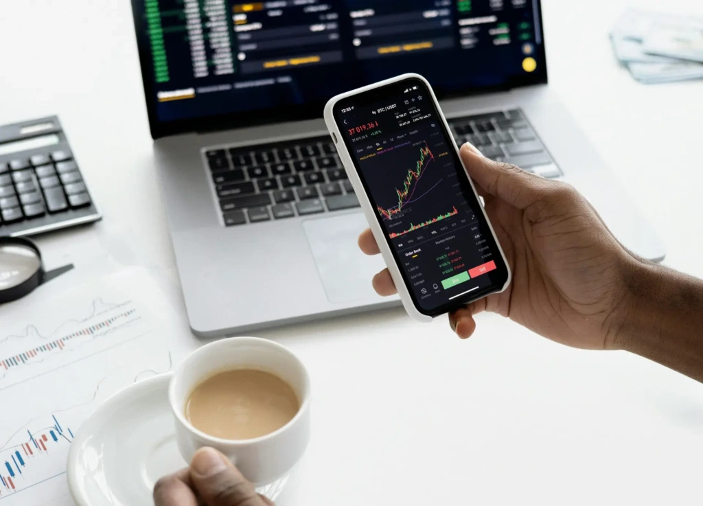 Bir kişi, mobil uygulama üzerinden kripto para grafiklerini incelerken aynı anda dizüstü bilgisayar ekranında piyasa verilerini takip ediyor.