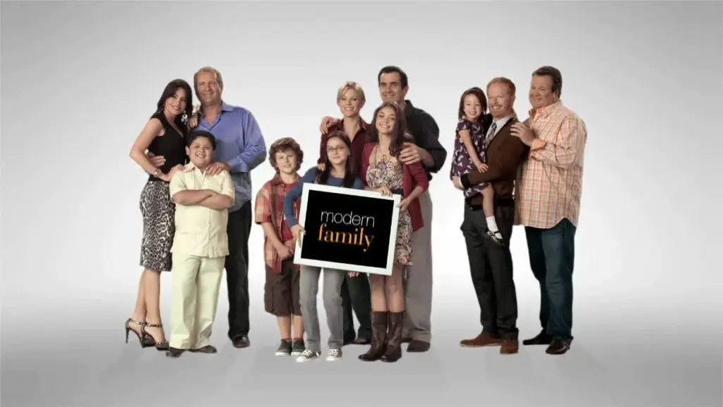 Modern Family dizisinin ana karakterleri beyaz arka plan önünde bir araya gelmiş, klasik aile portresi pozu veriyor.