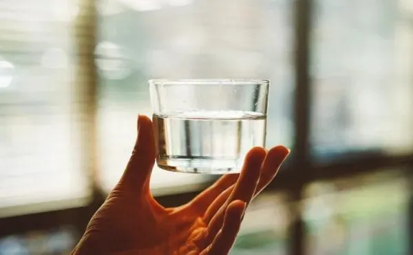 Gün ışığında cam bardakta tutulan su; sade yaşam, arınma ve sağlıklı rutinleri simgeleyen minimal wellness temalı görsel.