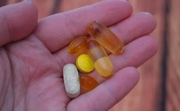 Elde tutulan çeşitli vitamin ve takviye kapsülleri; B12, D vitamini ve omega-3 gibi vegan yaşamda dikkat edilmesi gereken destekleyici besin öğeleri.