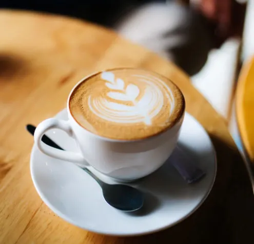 Beyaz fincanda latte art süslemeli cappuccino, tabağı ve kaşığıyla servis edilmiş