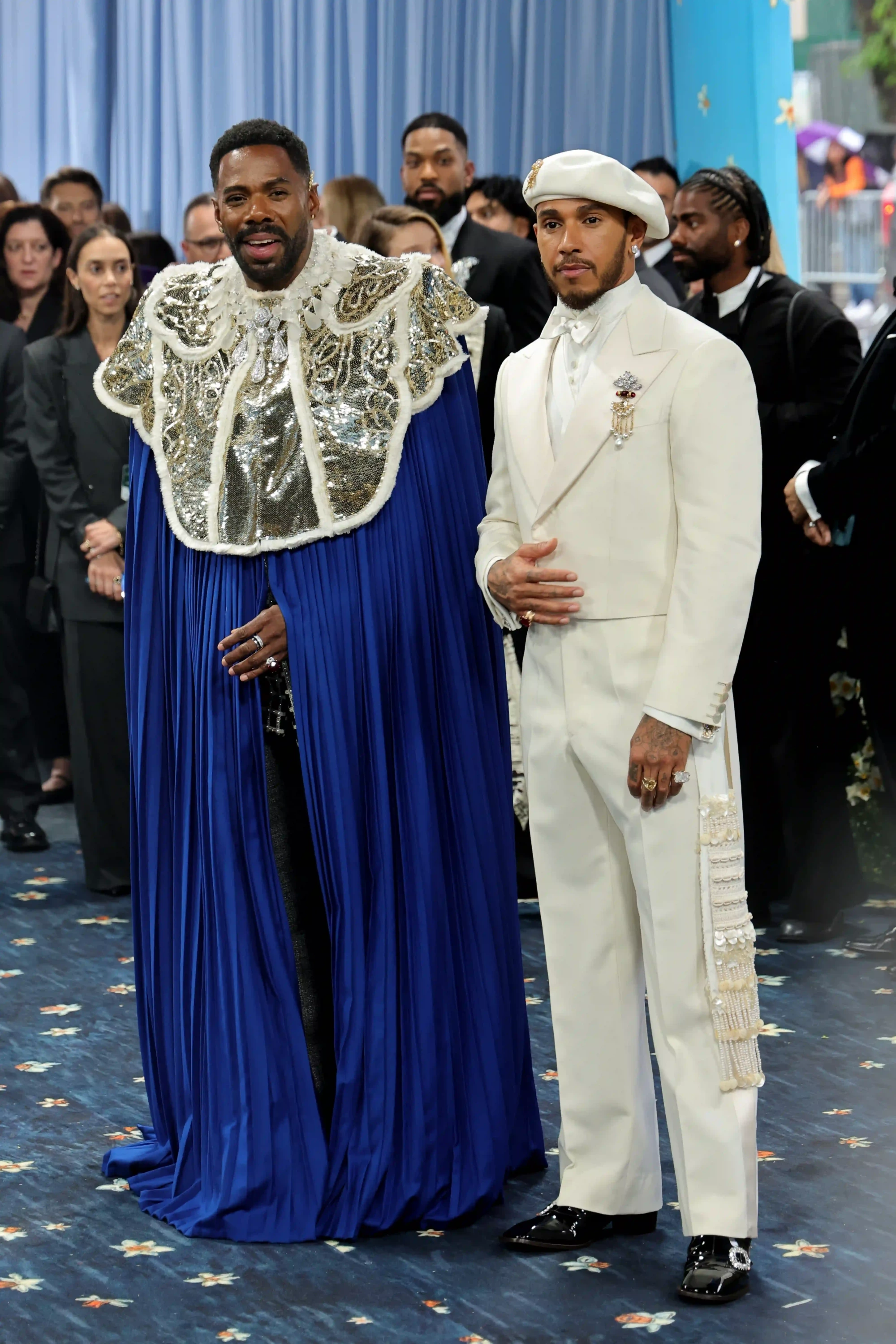 Colman Domingo, kraliyet mavisi işlemeli pelerini ve Lewis Hamilton ise beyaz zarif takım elbisesi, beresi ve incilerle süslenmiş aksesuarıyla 2025 Met Gala’da moda dünyasının dikkat çeken tasarımlarını sergileyerek etkinliğin ev sahipleri olarak göz kamaştırıyor.