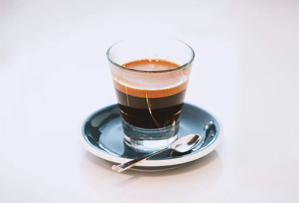 Cam bardakta espresso shot, tabağı ve kaşığıyla servis edilmiş siyah kahve