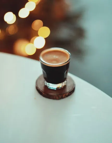 Ahşap altlık üzerinde küçük cam bardakta servis edilen espresso shot