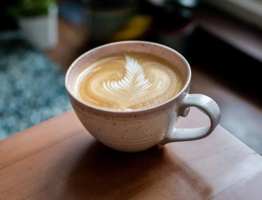 “Seramik fincanda latte art süslemeli flat white kahve, ahşap masa üzerinde