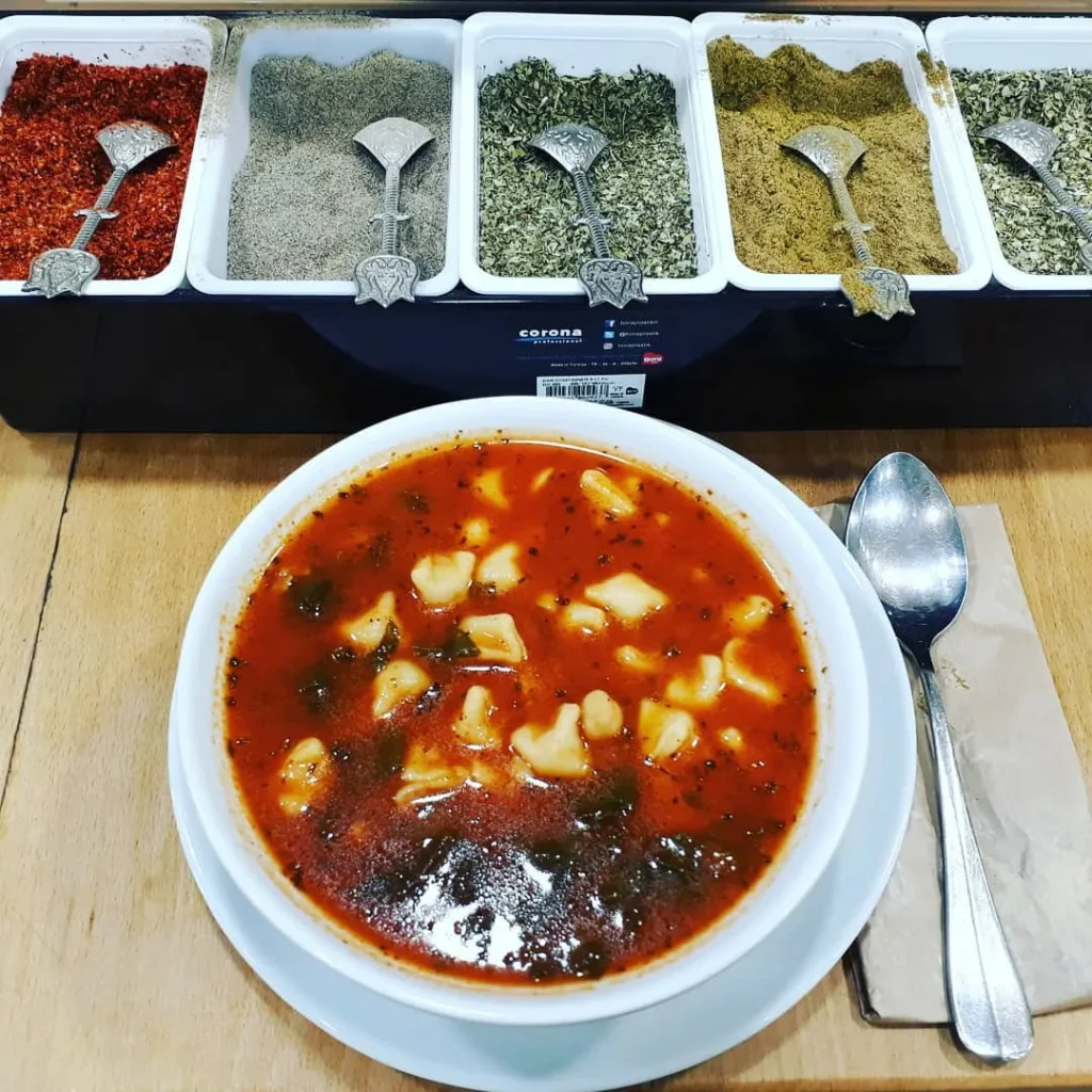 İstanbul Sanayi Mahallesi Hebun Çorba Evi’nde kırmızı renkli mantılı çorba, baharat barı önünde servis edilmiş