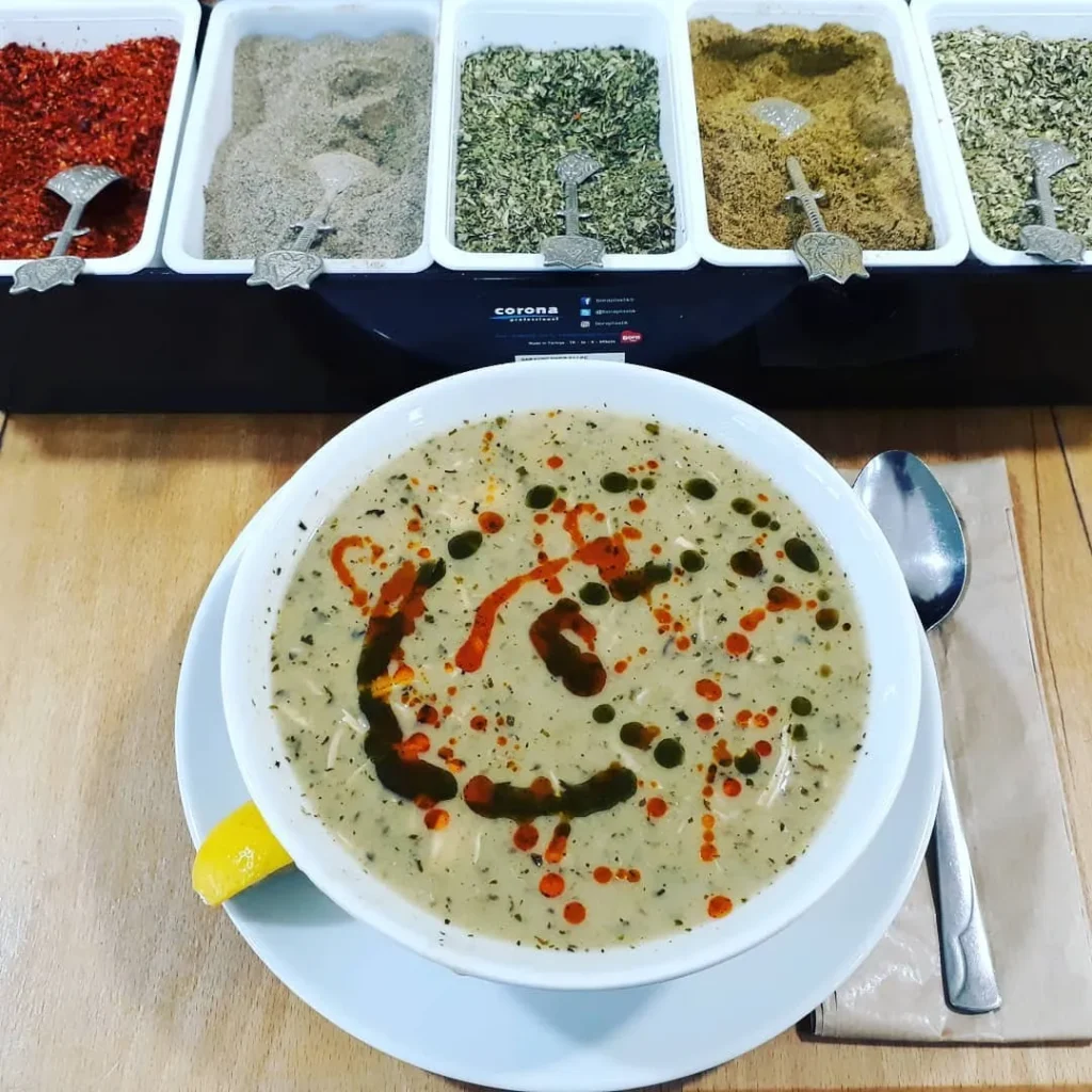 Hebun Çorba Evi’nde servis edilen mercimek çorbası, üzerine nane ve kırmızı yağ gezdirilmiş, yanında kaşık ve limonla sunulmuş.