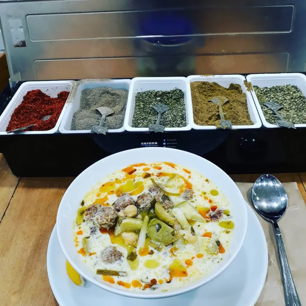 Sanayi Mahallesi Hebun Çorba Evi’nde sunulan sebzeli köfte çorbası, yanında çeşitli baharatlar ve limon dilimiyle servis edilmiş.