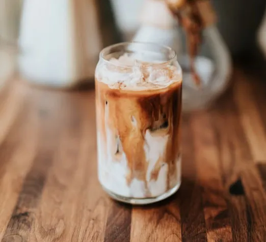 Cam bardakta buzlu latte macchiato, süt ve kahve katmanlarıyla ahşap masa üzerinde