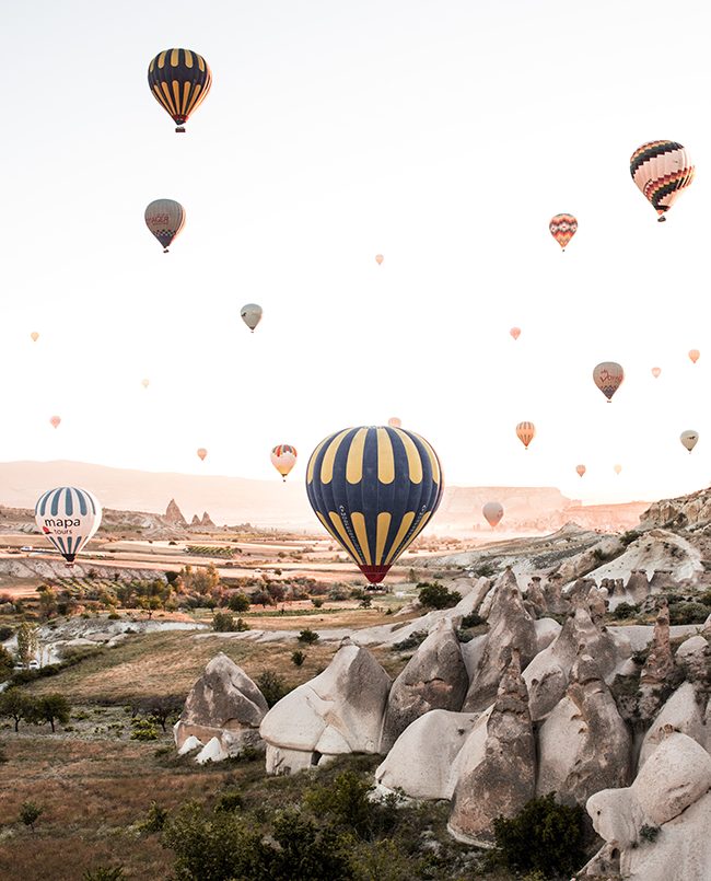 Kapadokya’da sabah gün doğumunda gökyüzünde süzülen sıcak hava balonları ve peri bacalarının panoramik manzarası