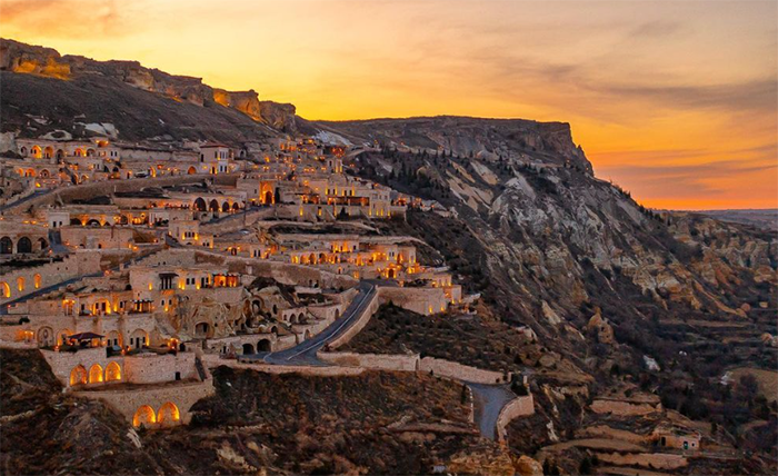 Kapadokya’da gün batımında ışıklarıyla parlayan Kayakapı Premium Caves otel ve vadinin panoramik manzarası