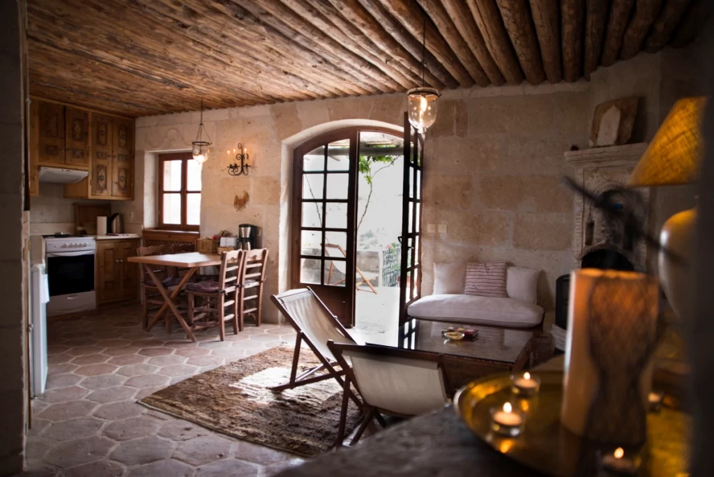 Les Maisons de Cappadoce’de taş duvarlı, rustik mobilyalarla döşenmiş oturma ve mutfak bölümü