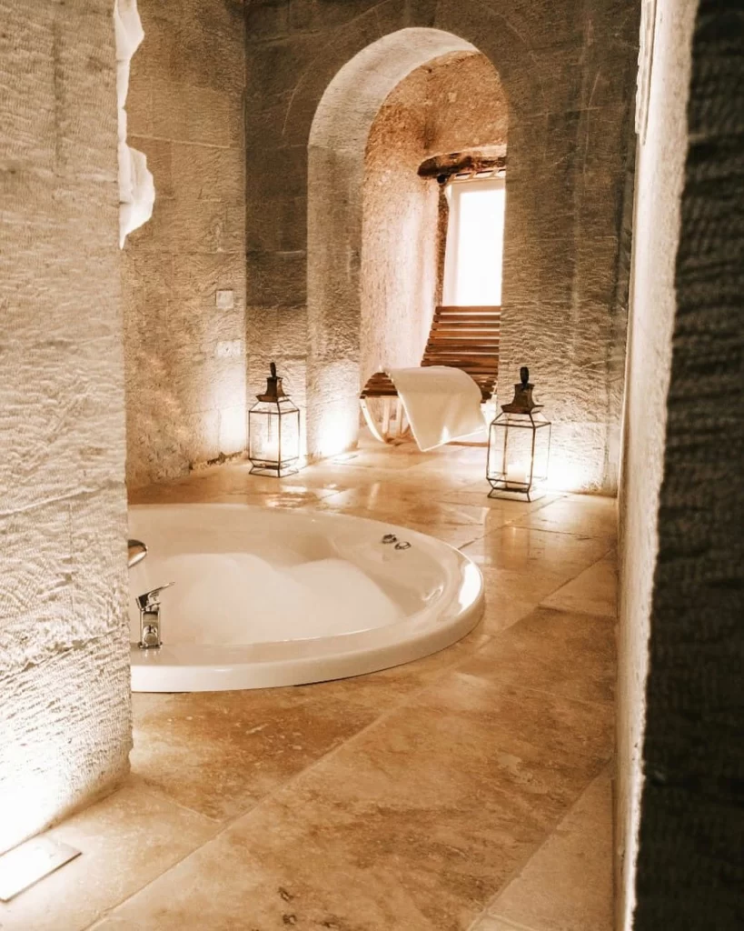 Millstone Cave Suites otelinin taş duvarlarla çevrili jakuzili banyosu ve loş ışıklı atmosferi