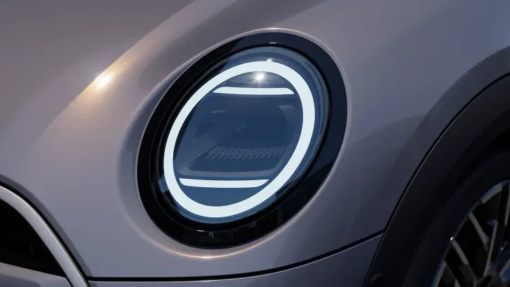 Şehir sokaklarında özgür sürüş deneyimi sunan Yeni MINI Cooper Cabrio'nun, markanın ikonik kimliğini koruyan ve günümüz estetiğiyle buluşan parlak beyaz LED aydınlatmalı yuvarlak ön farının detaylı yakın çekimi, modern retro ruhunu yansıtıyor.