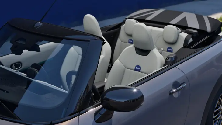 Parlak gümüş rengi Yeni MINI Cooper Cabrio'nun açılır tavanı tamamen açık haldeyken, aracın modern bej renkli koltukları ve katlanmış, Union Jack desenli şık tavan kumaşı net bir şekilde görülüyor ve bu ikonik modelin sunduğu her an özgür açık hava sürüş deneyimini gözler önüne seriyor.