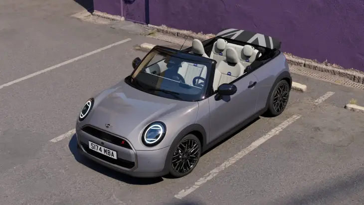 Gri renkli yeni MINI Cooper Cabrio, açık tavanı ve beyaz iç mekanıyla bir otoparkta park halinde görülüyor; katlanmış tavanındaki ikonik Union Jack deseni ve modern LED farlarıyla dikkat çeken bu model, her an özgür bir sürüş deneyimi vadediyor.