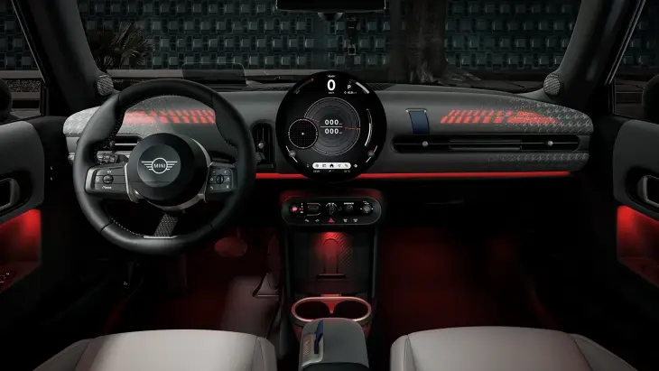 Yeni MINI Cooper Cabrio'nun iç mekanında, direksiyonun arkasından görünen, merkezde yer alan büyük dairesel OLED ekran hız, yakıt ve diğer sürüş bilgilerini gösterirken, ön konsolu ve ayak boşluklarını aydınlatan kırmızı ambiyans ışıkları modern ve dijital bir sürüş deneyimi sunarak her an özgür bir his yaratıyor.