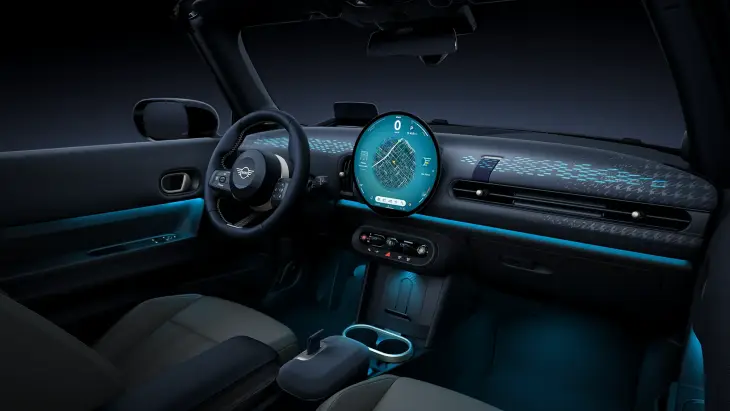 Yeni MINI Cooper Cabrio modelinin karanlık iç mekânında, parlak dairesel OLED ekranın gösterdiği navigasyon haritası, mavi ambiyans aydınlatmaları ve modern dashboard tasarımıyla dijital konfor ve özgür sürüş deneyimi vurgulanmaktadır.