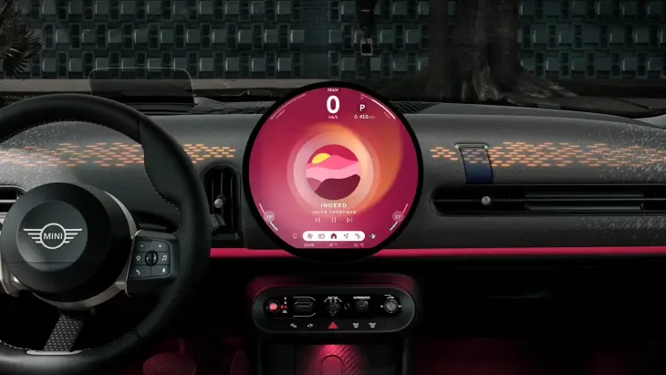 Yeni MINI Cooper Cabrio modelinin kokpitinden bir görünümde, araç dururken 'Indeed' şarkısını çalan büyük dairesel OLED ekran, ön paneldeki altıgen desenli ışıklandırmalar ve direksiyon simidiyle modern ve özgür bir sürüş deneyiminin dijital konforunu sergiliyor.
