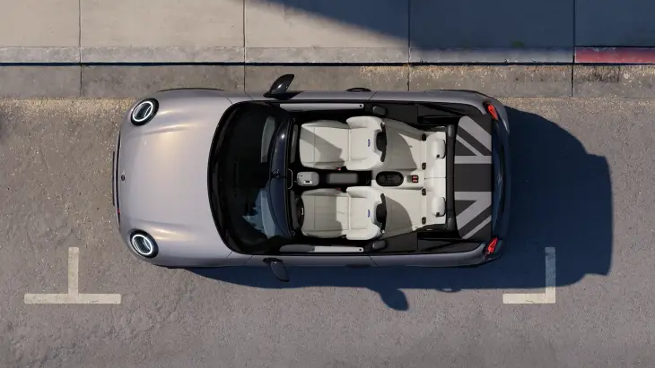 Açık tavanlı gümüş rengi Yeni MINI Cooper Cabrio, üstten çekilmiş bir karede gri asfalt zeminde park halinde görülüyor; beyaz koltuklara sahip iç mekanı ve arka kısımda Union Jack deseni işlenmiş tavan saklama alanı dikkat çekerken, her an özgür bir sürüş deneyimi vadeden bu model, açık havanın ve çağdaş stilin tadını çıkarmak isteyenlere hitap ediyor.