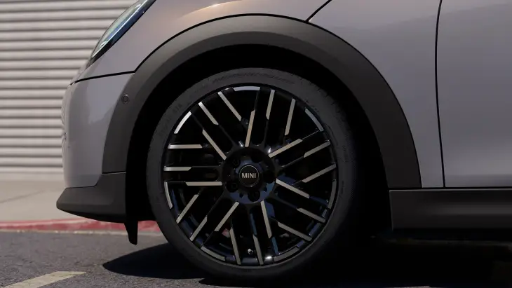 Gri renkli yeni MINI Cooper Cabrio modelinin dinamik ve modern dış tasarımını sergileyen, mat siyah ve parlak metalik detaylarla bezenmiş çok kollu jantlara sahip ön tekerleği ve estetik çamurluk ağzı, her an özgür bir sürüş için göz alıcı bir davet sunuyor.