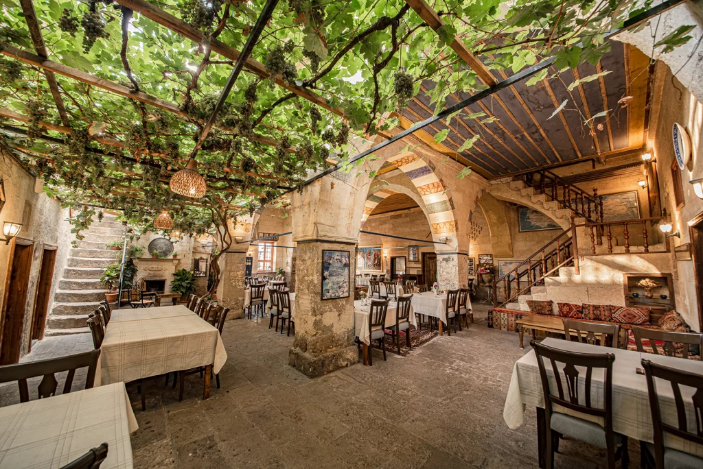 Old Greek House’un asma yapraklarıyla örtülü avlusu ve taş mimarili restoran alanı – Kapadokya