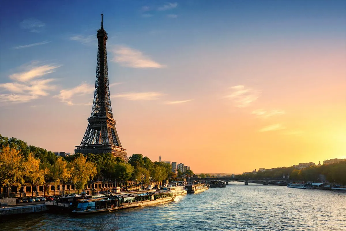 Paris’te Eyfel Kulesi ve Seine Nehri’nin gün batımında, ağaçlarla çevrili kıyılar ve teknelerle birlikte görünen manzarası.