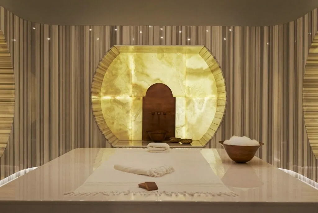Raffles İstanbul’daki Raffles Spa’nın altın tonlu modern Türk hamamı alanı; mermer göbek taşı, aydınlatmalı duvar tasarımı ve köpük ritüeli detaylarıyla lüks bir spa deneyimi sunuyor.